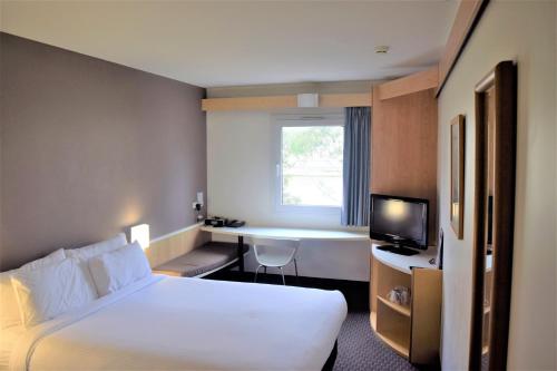 Habitación de hotel con cama, escritorio y TV. en ibis Thornleigh, en Thornleigh