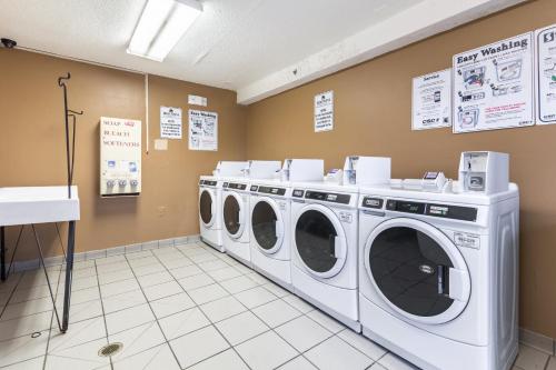 a laundry room with three washing machines and signs on the wall at HomeTowne Studios by Red Roof Louisville in Louisville