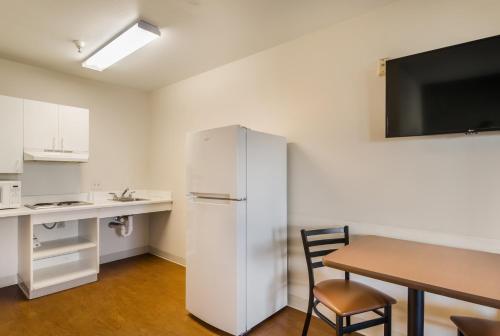 a kitchen with a white refrigerator and a table and a desk at HomeTowne Studios by Red Roof Denver - Airport/Aurora in Aurora