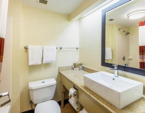 a bathroom with a sink and a toilet and a mirror at Red Roof Inn PLUS+ West Palm Beach in West Palm Beach