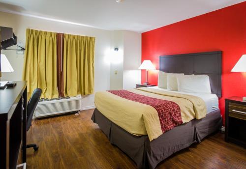 a hotel room with a bed and a red wall at Red Roof Inn Austin - Round Rock in Round Rock