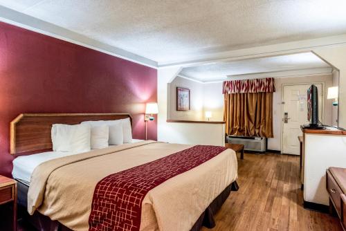 a hotel room with a large bed with a red wall at Red Roof Inn & Suites Clinton, TN in Clinton