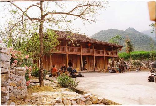 a large wooden house with people sitting outside of it at Lo Lo Homestay & Cafe Meo Vac in Mèo Vạc