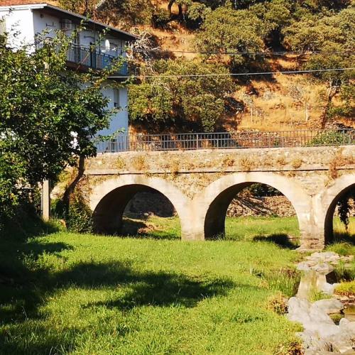 a bridge over a river in a grassy field at Casa Rural El Chorritero in Ovejuela