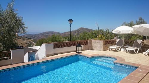 a swimming pool with chairs and umbrellas next to at Casa Rural Las Molina in Frigiliana