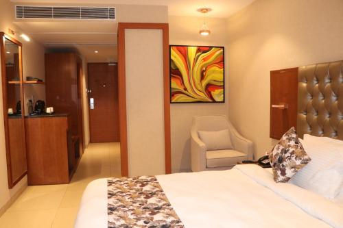 a bedroom with a bed and a chair and a painting at SK Lords Inn Ahmedabad in Ahmedabad