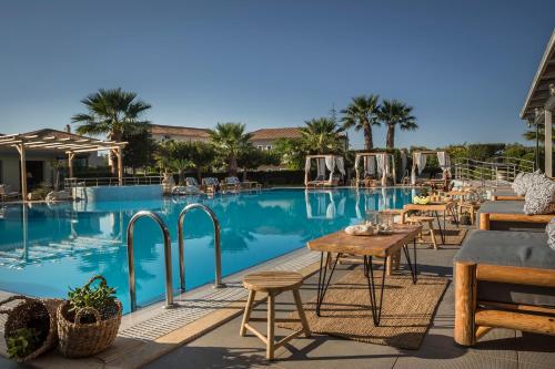 a pool with tables and chairs and palm trees at Avithos Resort Hotel in Svoronata