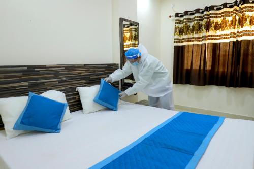 a man in a whitensicsnsicsnsicsnsicsnsics officer preparing a bed with blue at Perfectstayz Value Umra Grace - Near Haridwar Railway Station in Haridwār
