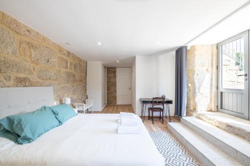 - une chambre avec un grand lit blanc et un mur en pierre dans l'établissement Casa da Veiga, à Aldeia