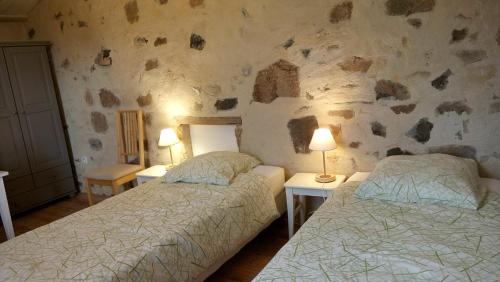 - 2 lits dans une chambre avec un mur en pierre dans l'établissement La Pierre Folle Chambres d'Hôtes, à Cluny