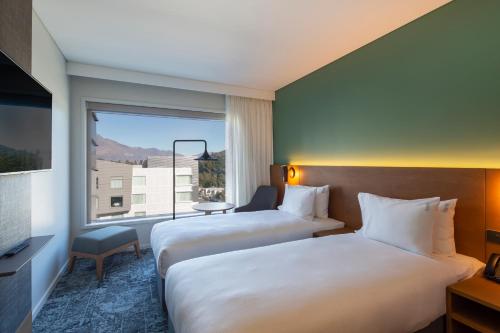 two beds in a hotel room with a window at Holiday Inn Express & Suites Queenstown by IHG in Queenstown