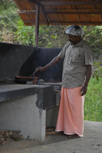 a man standing next to a grill with a pan at Beyond Eco Living in Munnar