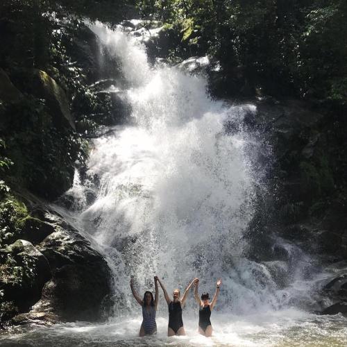 three people standing in the water in front of a waterfall at Finca Carpe Diem Ecolodge in Minca