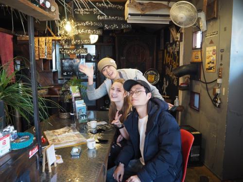 three people sitting at a table in a bar at 民泊カフェ Gootarian in Kumamoto