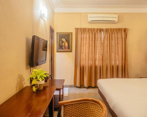 Cette chambre comprend un lit, un bureau et une télévision. dans l'établissement Hanu Reddy Residences Wallace Garden, à Chennai