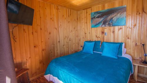 1 dormitorio con 1 cama azul en una pared de madera en ELUNEY Pichilemu en Pichilemu