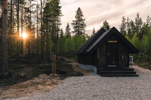a small cabin in the woods with the sun setting at Aurora Village Ivalo in Ivalo