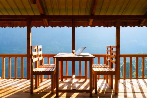 a table and two chairs on a porch with a laptop at Zostel Shangarh, Kullu in Sainj