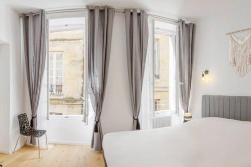 a bedroom with a white bed and two windows at Logement de charme - Porto Riche - Cœur historique Bordeaux in Bordeaux