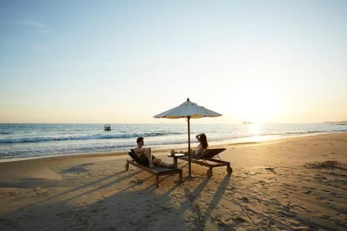 two people sitting on the beach under an umbrella at Centara Q Resort Rayong in Mae Pim