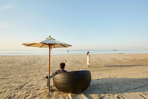 a man sitting in a chair under an umbrella on the beach at Centara Q Resort Rayong in Mae Pim