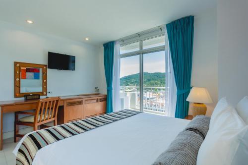 a bedroom with a bed and a desk and a window at Waterfront Suites Phuket by Centara in Karon Beach