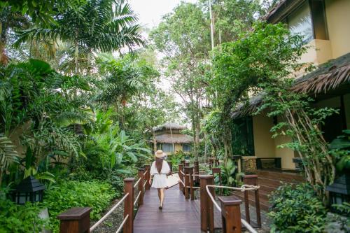 a woman walking down a wooden walkway through a garden at Centara Koh Chang Tropicana Resort in Ko Chang
