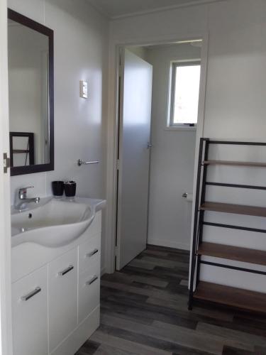 een badkamer met een wastafel, een spiegel en een ladder bij Karoro the beach front bach with views to die for! in Raglan