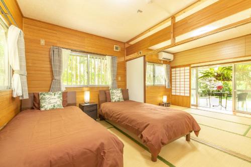 two beds in a room with wooden walls and windows at Villa Itona in Ishigaki Island