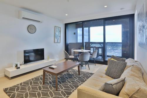 a living room with a couch and a tv and a table at Box Hill Central Sky One Apartment in Box Hill
