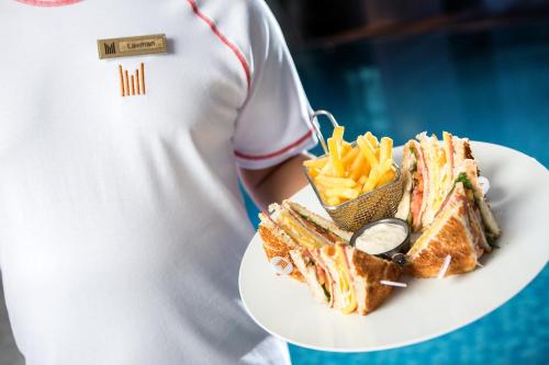 a person holding a plate with a sandwich and french fries at Millennium Kurdistan Hotel & Spa in As Sulaymānīyah