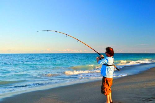 a man standing on a beach holding a fishing rod at Astrofegia Apartments Near The Sea in Ayia Marina