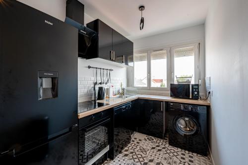 a kitchen with black cabinets and a washer and dryer at Le Grand Drancy - 3 chambres - tout équipé in Drancy