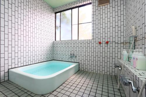 a white tiled bathroom with a tub and a window at Lake Oshino in Oshino