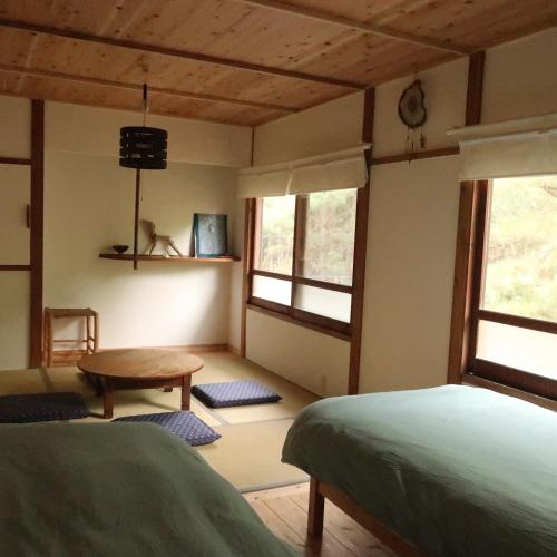 a bedroom with a bed and a table and windows at 奈多みどり荘 Nada Beach House in Kitsuki