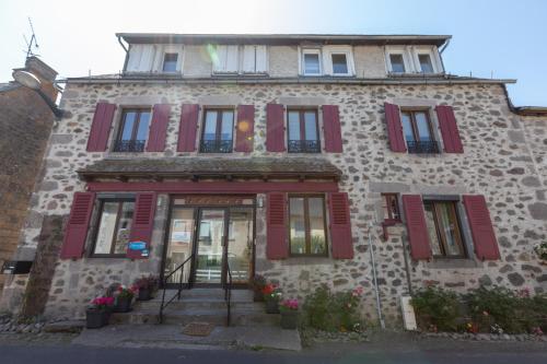 a stone building with red shutters and a door at La Belle Arverne in Albepierre-Bredons