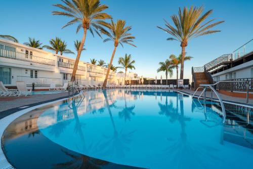 a large swimming pool with palm trees in the background at Plus Fariones Apartamentos in Puerto del Carmen