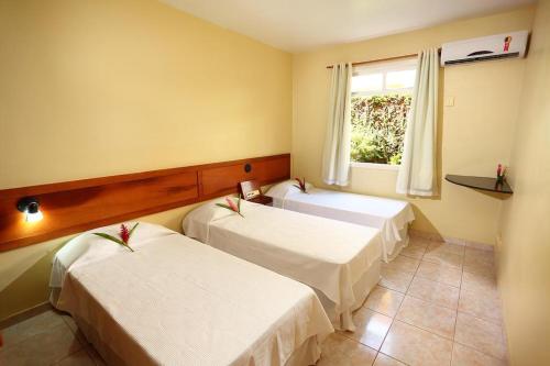 two beds in a room with a window at Boulevard da Praia Apart Hotel - Porto Seguro - Frente da Praia de Taperapuan in Porto Seguro