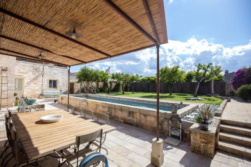 patio con mesa de madera, sillas y piscina en Antica Dimora Giardini Segreti, en Giuggianello