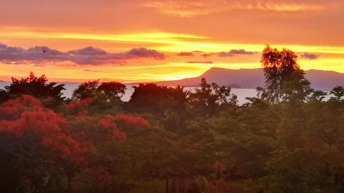 a sunset over a forest of trees with mountains in the background at Q Bungalows in Kep