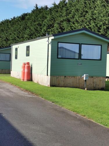 a green and white building with a fence and a house at Woofles Luxury Caravan at Knaresborough Lido in Knaresborough