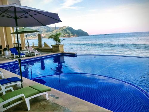a swimming pool with chairs and an umbrella and the ocean at Hotel Bogavante in Barra de Navidad