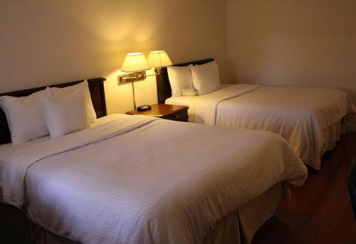 a hotel room with two beds with white sheets at Days Inn & Suites by Wyndham Sunnyvale in Sunnyvale