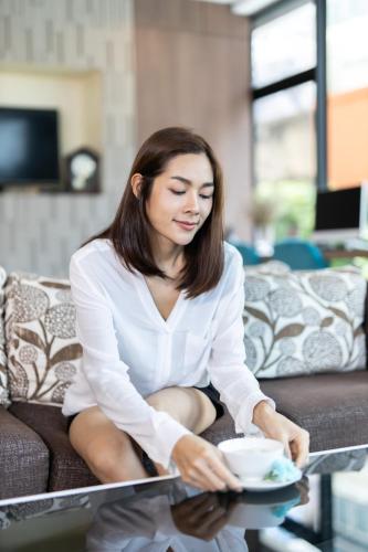 a woman sitting on a couch with a cup of coffee at The Centris Hotel Phatthalung in Phatthalung