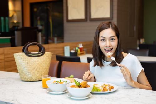 a woman sitting at a table eating food with a fork at The Centris Hotel Phatthalung in Phatthalung