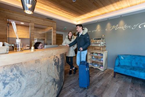 a man and woman standing at a bar with a suitcase at Mont Chalet Nevada - Hotel & Spa in Livigno