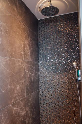 a bathroom with a shower with brown tiles at Harbour Suites Boutique Hotel in Monnickendam