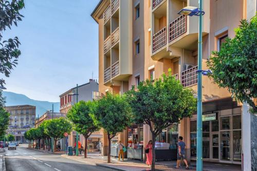 a city street with a tall building and trees at Résidence Pierre & Vacances Les Citronniers in Menton