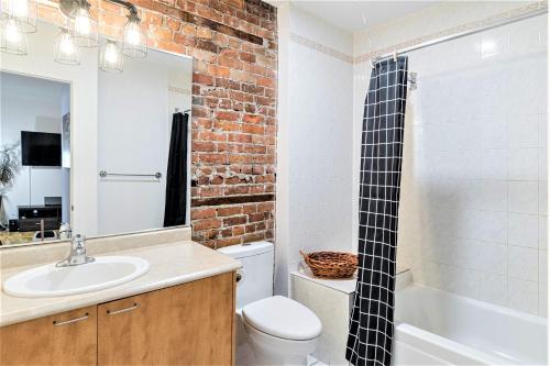 a bathroom with a white sink and a brick wall at Le Théâtral - En plein coeur de l'action avec stationnement in Quebec City