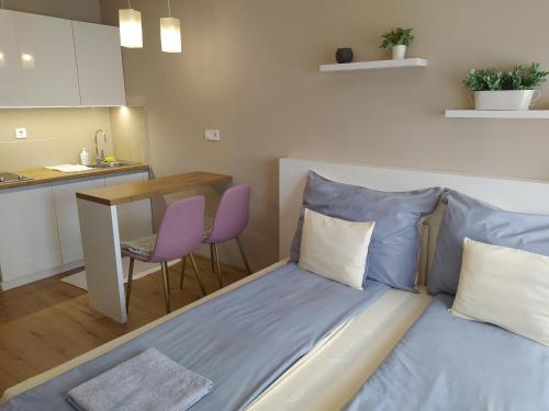 a bed in a room with a table and a kitchen at Lia Apartman in Nyíregyháza